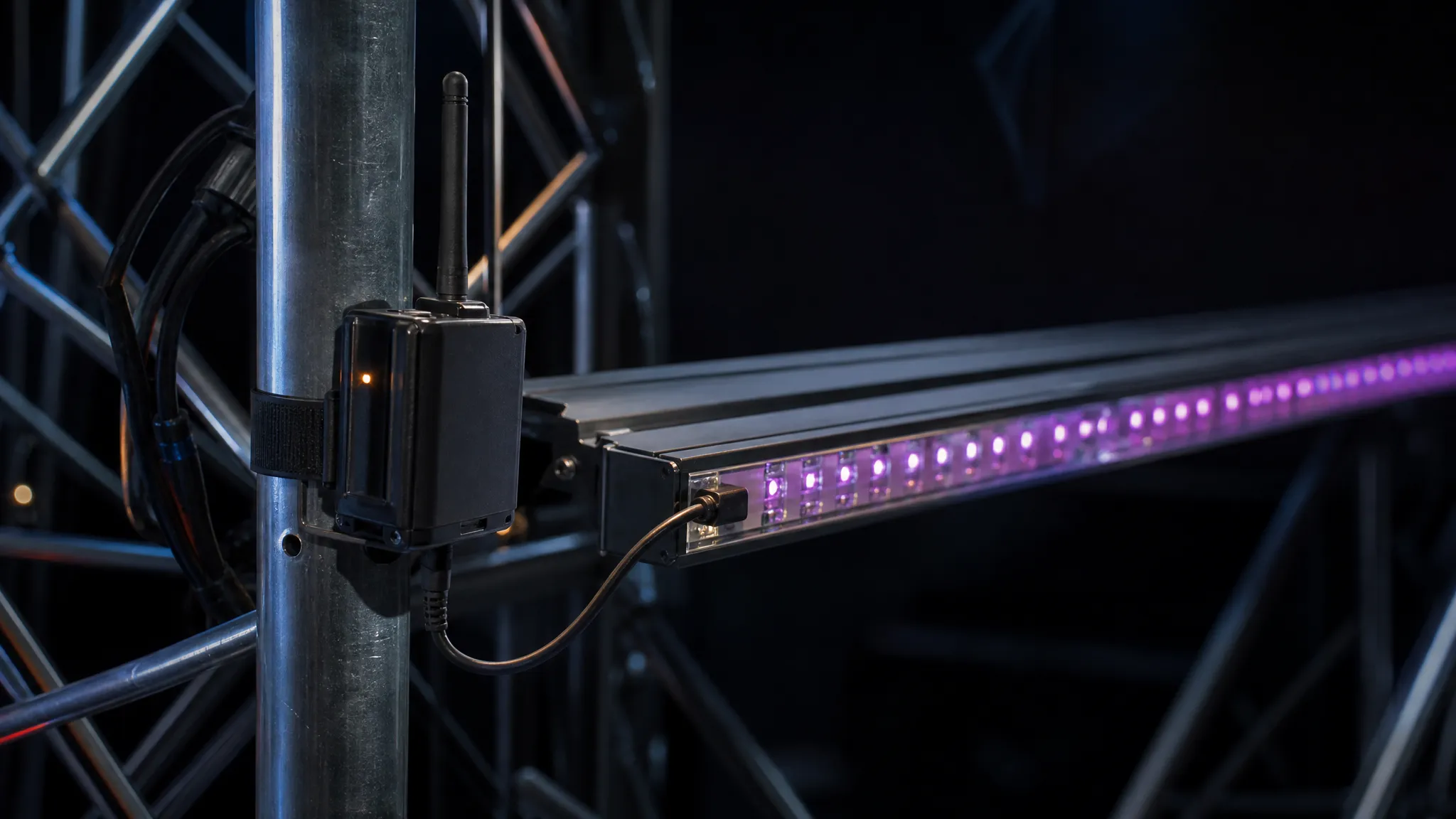 A battery-powered wireless DMX receiver clipped beside an addressable pixel strip, with a short DMX jumper cable looping to the strip's controller