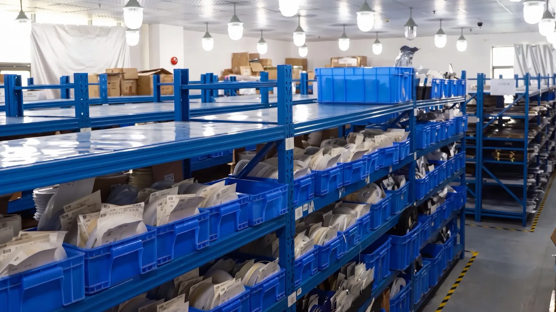 Racked blue bins of LED strip reels and components in the manufacturer's warehouse, the buffer stock that keeps a supply line continuous