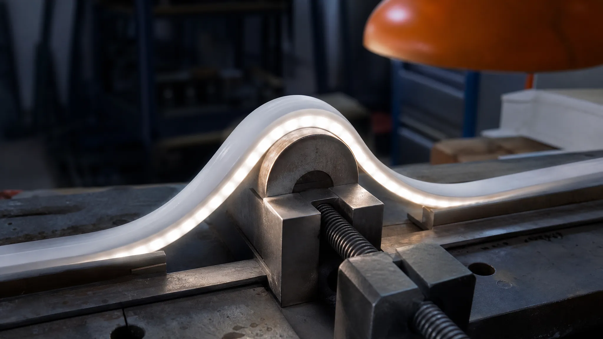 A lit white neon flex run bent to a tight radius in a workshop jig, at the apex where the inside face of the curve compresses