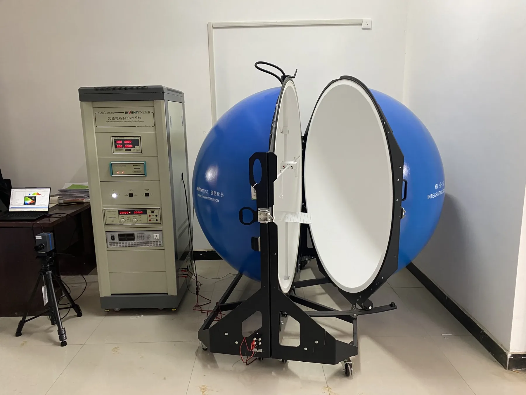 A two-meter integrating sphere opened for a color and output measurement, beside its control rack in a test room