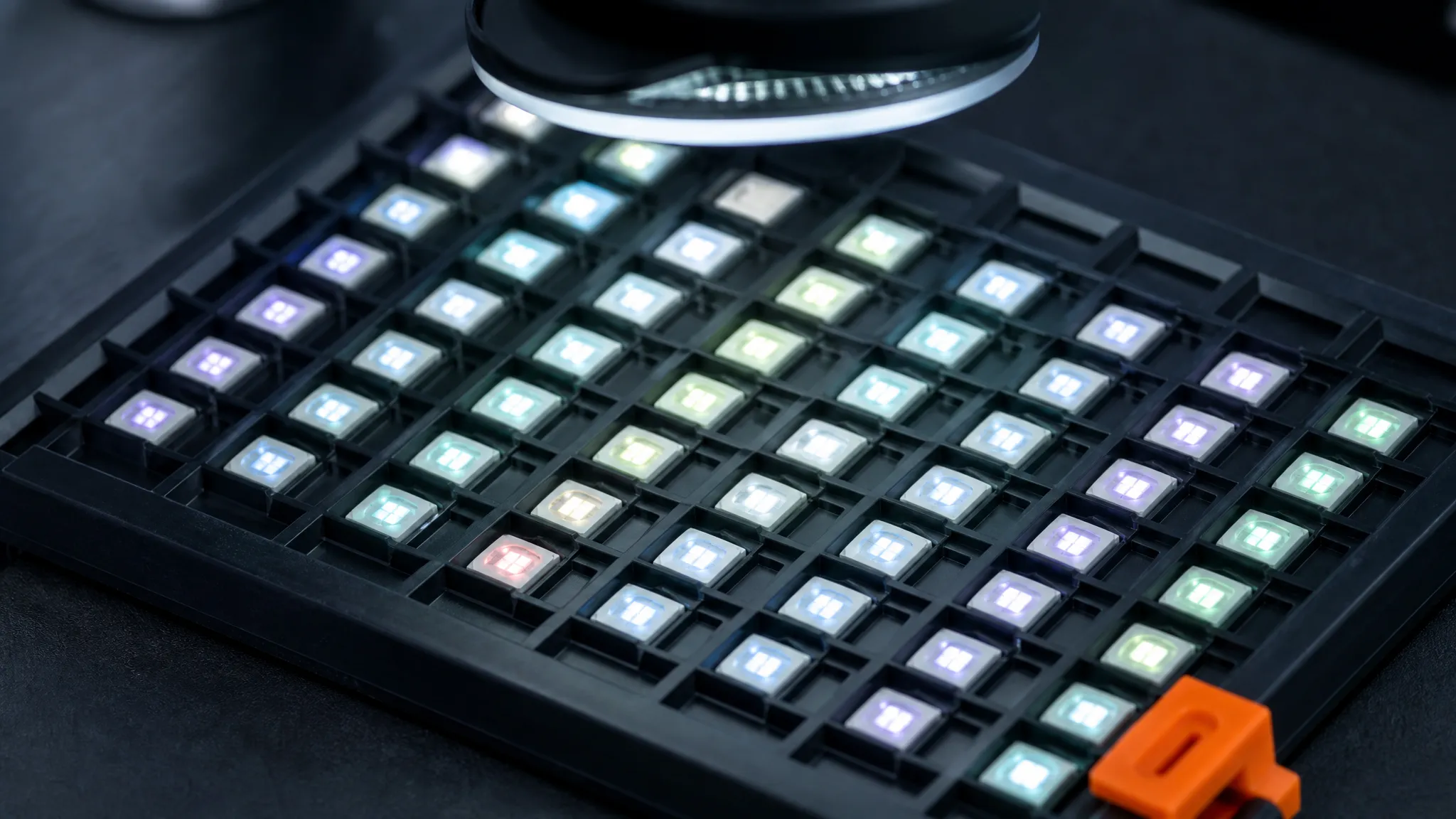 A tray of SMD RGB LED chips under a laboratory inspection lamp, with the lit chips showing a faint but visible difference in hue between adjacent parts