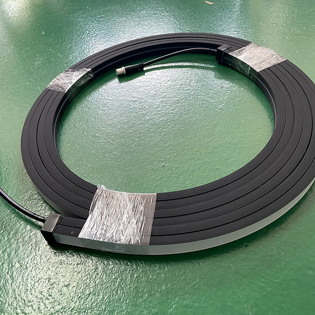 A finished silicone LED neon flex length coiled on a factory floor, showing the moulded end cap and the lead wire exiting the sealed end