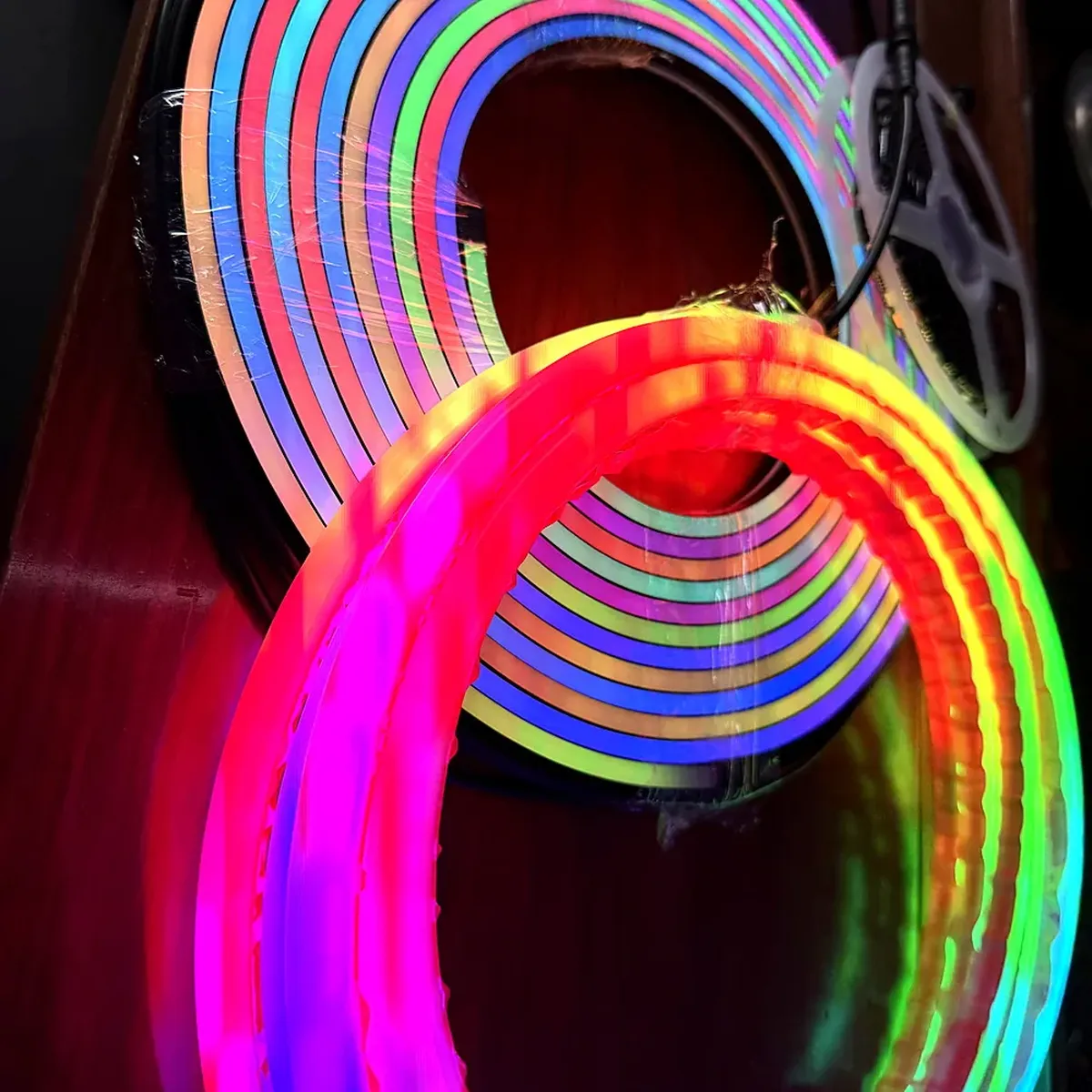 Several lit neon flex profiles of different colors coiled together on a dark background, showing how the cross-section and the jacket differ across one family