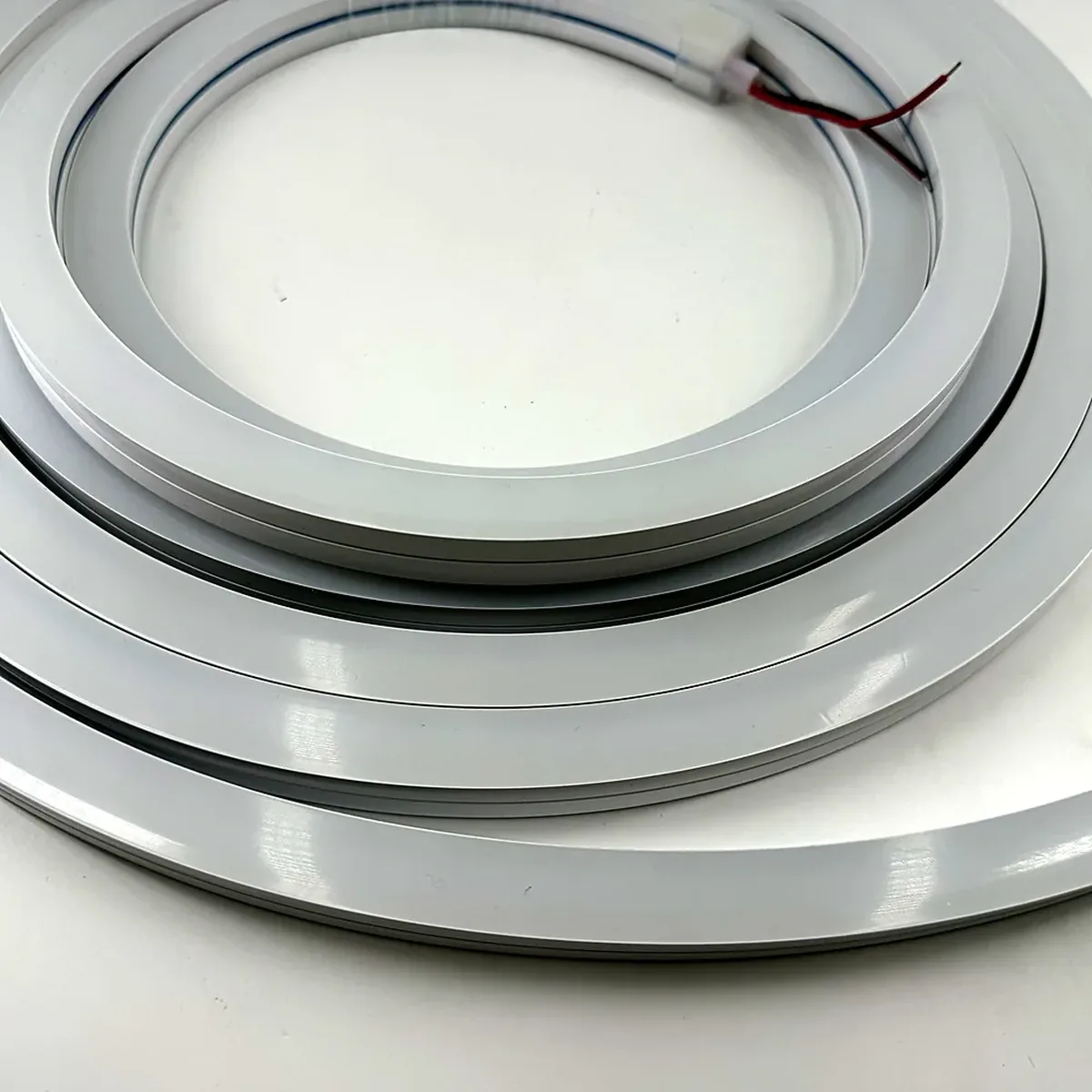 A close-up of the extruded side wall of unlit white LED neon flex, with one terminated end and its lead wires visible at the top of the frame