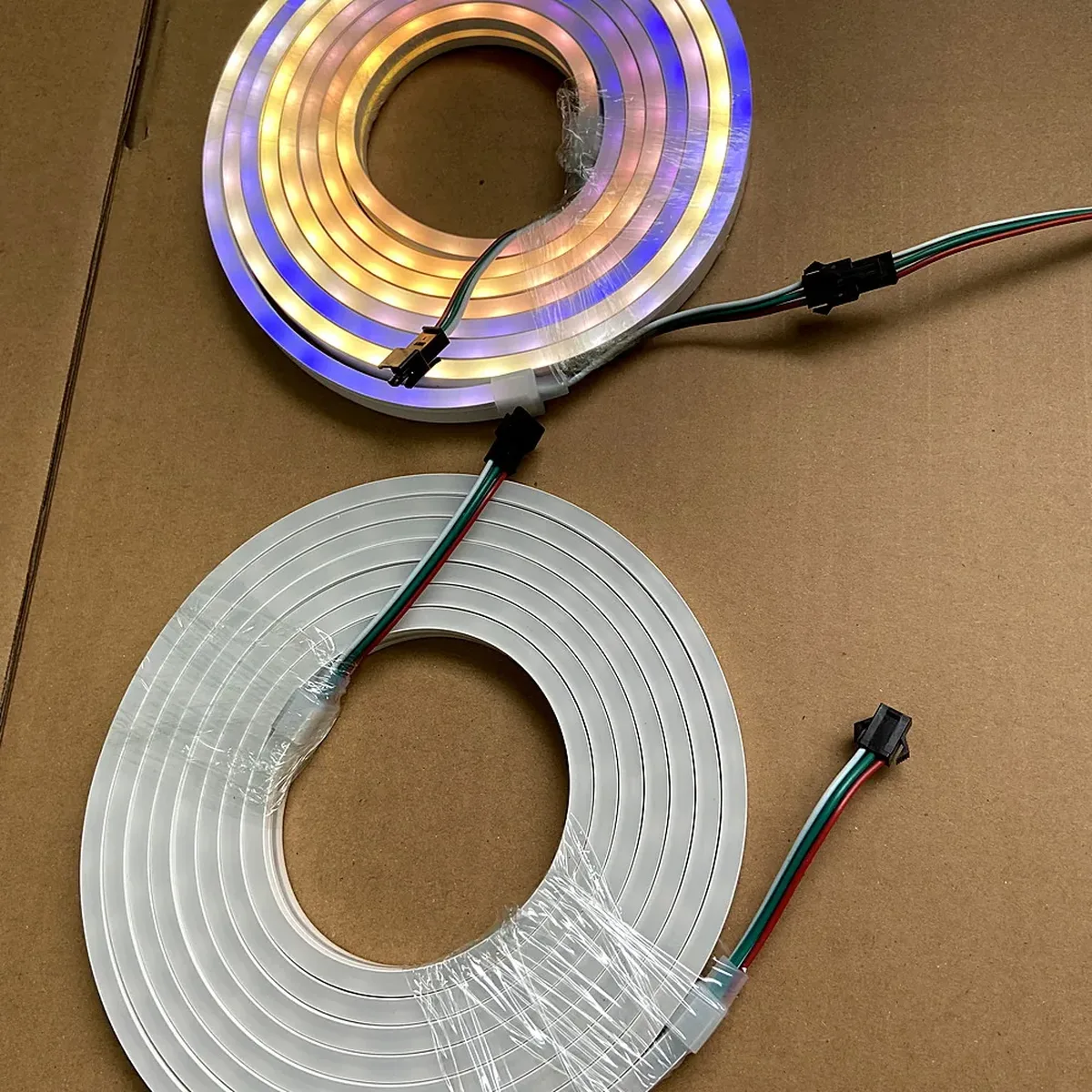 Two coiled lengths of addressable LED neon flex on a workshop floor, each showing a sealed end with a lead wire and a plug connector