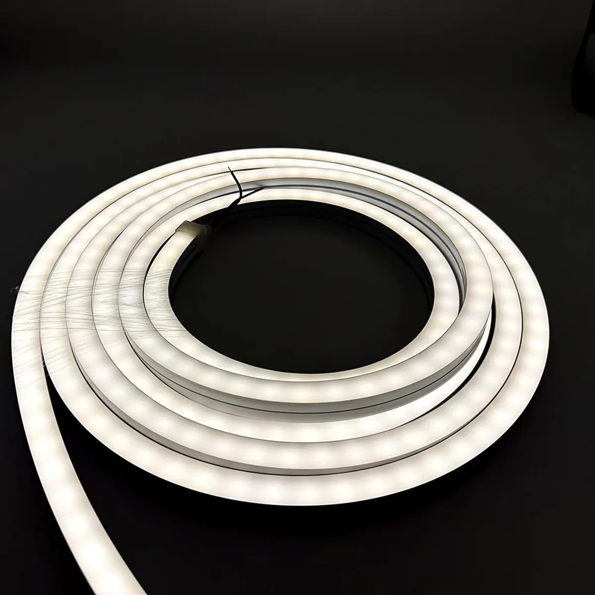 A lit white LED neon flex run coiled on a dark surface, its sealed end fitted with a moulded end cap and a thin lead wire