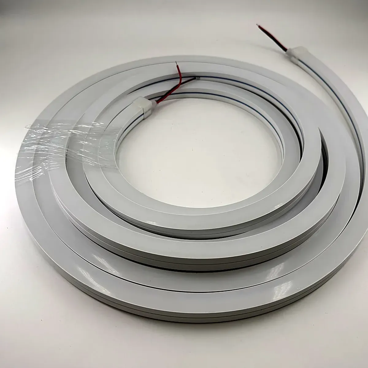 An unlit white silicone LED neon flex profile coiled into flat concentric loops on a tabletop, with the lead wires at the terminated end