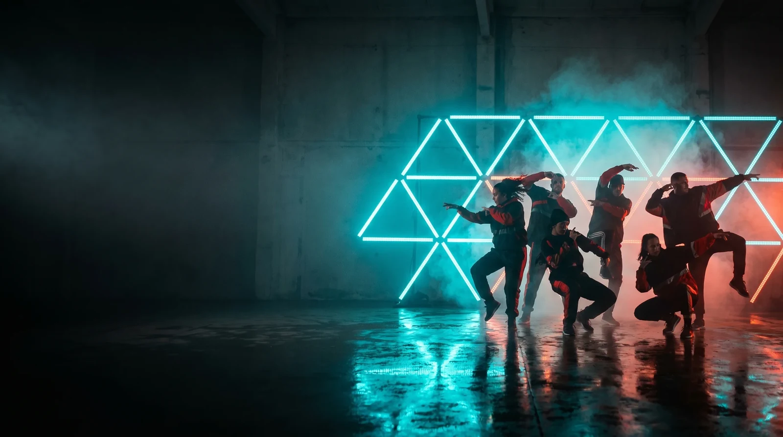 Performers silhouetted in front of a geometric pixel tube structure glowing teal on a dark fogged stage